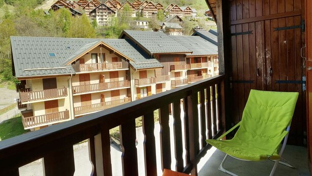 En balkong med utsikt över en rad trähus, en trädörr och en grön stol.