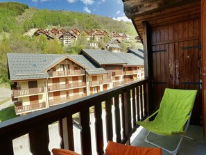 En balkon med udsigt over række af træhuse, en trædør og en grøn stol.