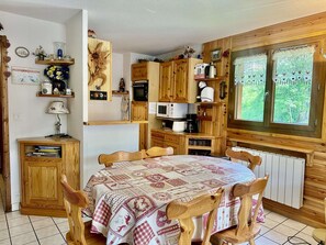 Una cuina acollidora amb armaris de fusta, taula de dinar i cadirees, i una finestra amb cortines.