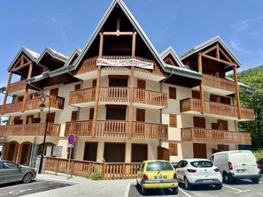 A multi-story building with balconies, a sign indicating no parking, and a parking area with cars. - Cozy central apartment - 5 guests (Valloire)
