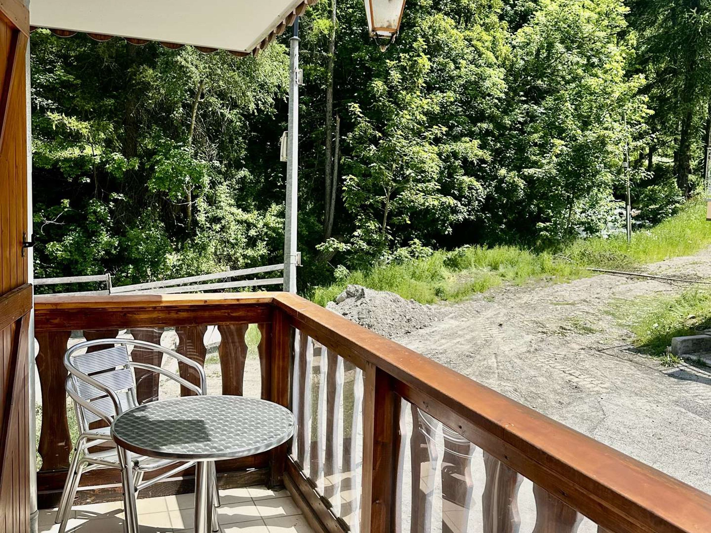 A wooden deck with a metal table and chairs, overlooking a dirt path and dense greenery.