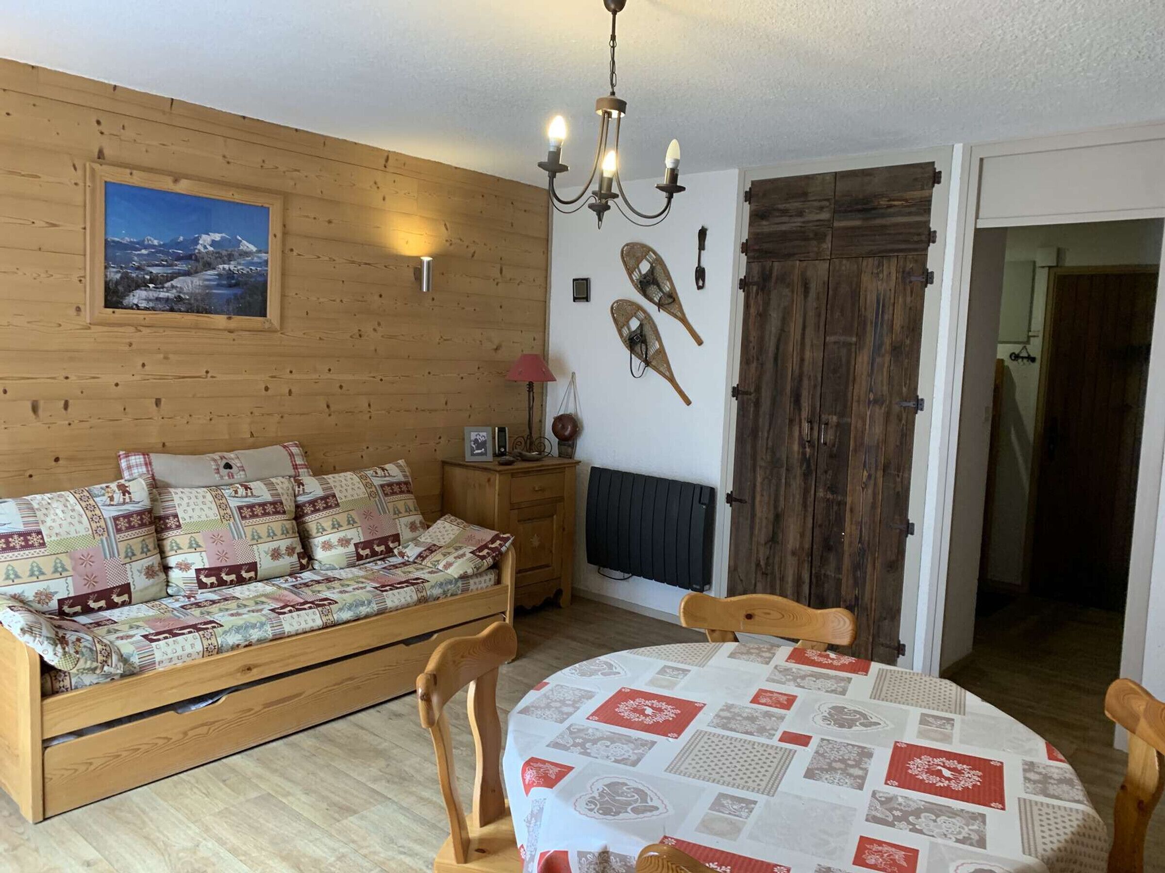 A cozy room with a wooden bed, a dining table with a quilt, a wooden door, and a wall-mounted picture.