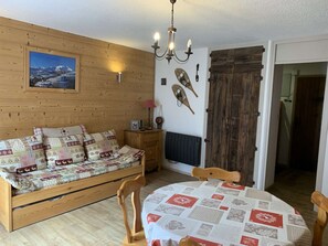 A cozy room with a wooden bed, a dining table with a quilt, a wooden door, and a wall-mounted picture. - Functional studio with cabin - 4 guests (Valloire)