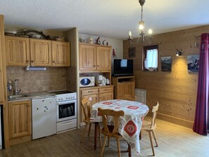 A cozy kitchen with wooden cabinets, a dining table with chairs, a microwave, a stove, and a television. - Functional studio with cabin - 4 guests (Valloire)