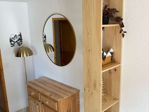 Ein Zimmer mit einem Holzkabinett, einem Spiegel, einer Lampe und einem Regal mit Dekorationen.