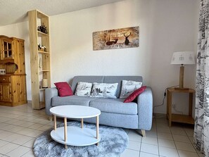 A living room with a grey sofa, a round white coffee table, a wooden cabinet, and a painting of deer on the wall. - Practical apartment near center - 6 guests (Valloire)
