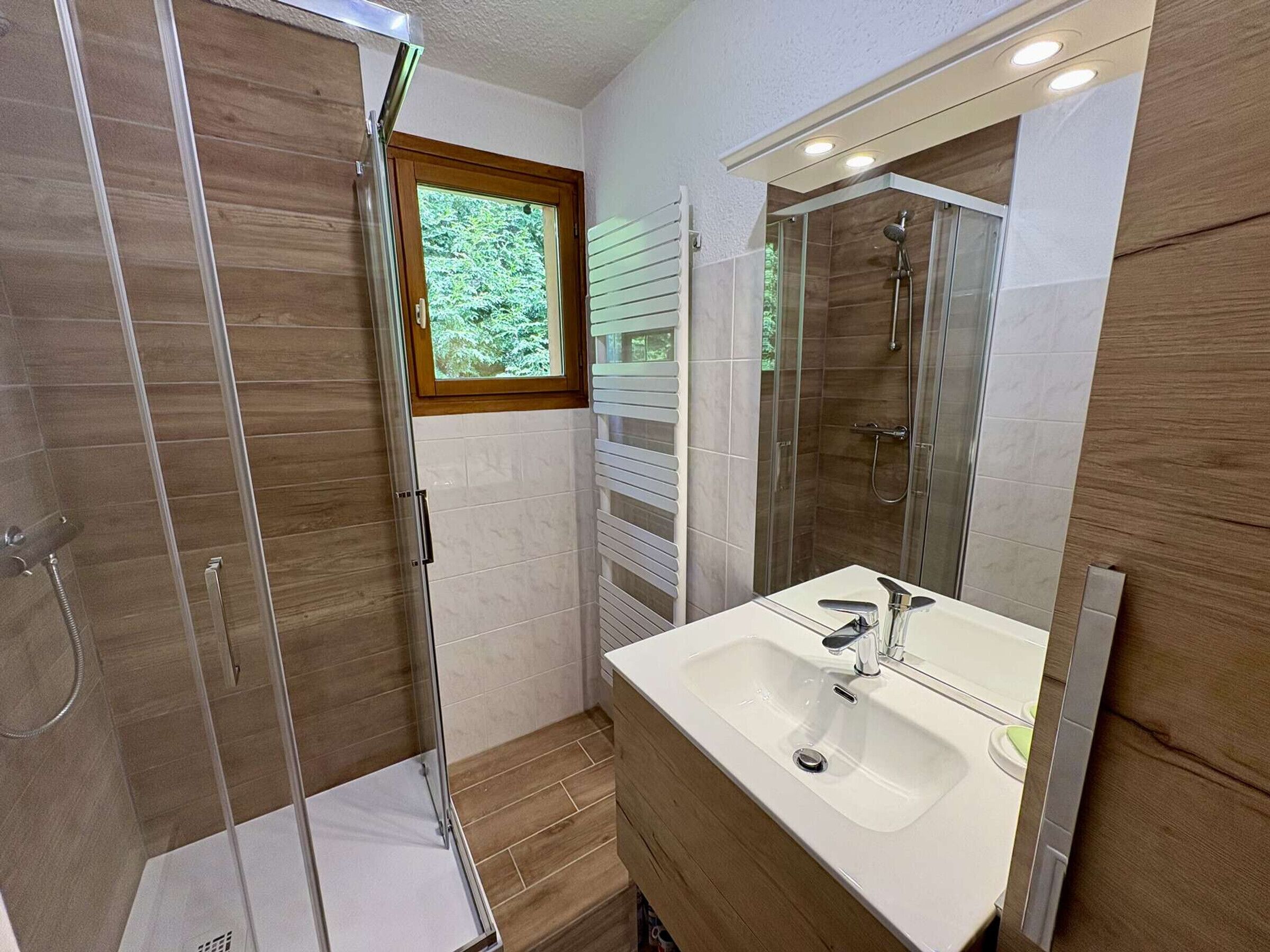 Een moderne badkamer met een douchecabine van glas, een grote spiegel en een witte wastafel.