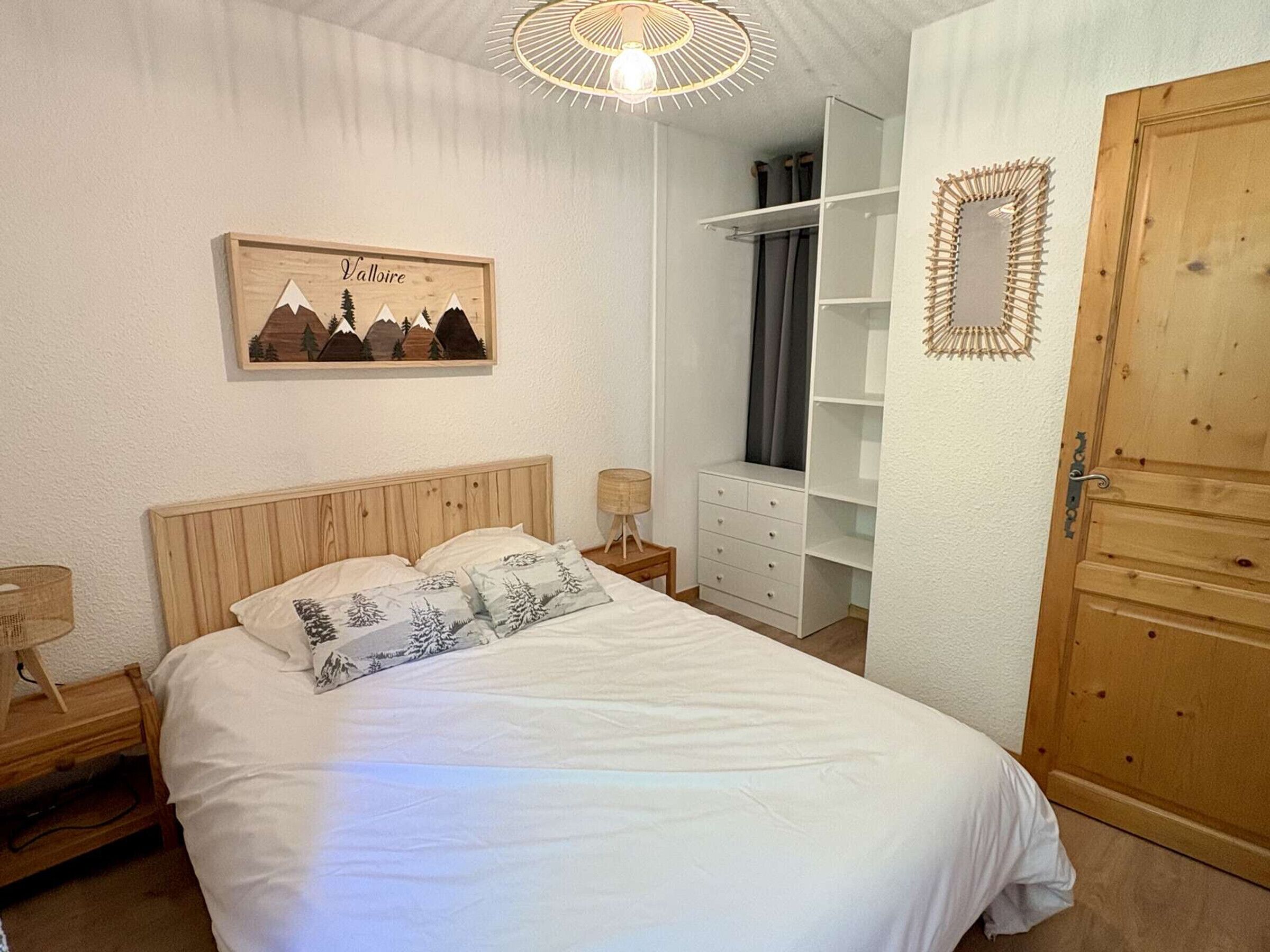 A bedroom with a wooden bed, a white wardrobe, a wooden door, and a wall-mounted mirror.