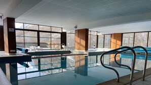 En inomhuspool med väggar av genomskinligt glas, en hoppställning och en poolstege.