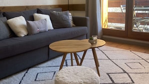 Ett modernt vardagsrum med en grå soffa, ett runt soffbord i trä och en vit, mjuk pall.
