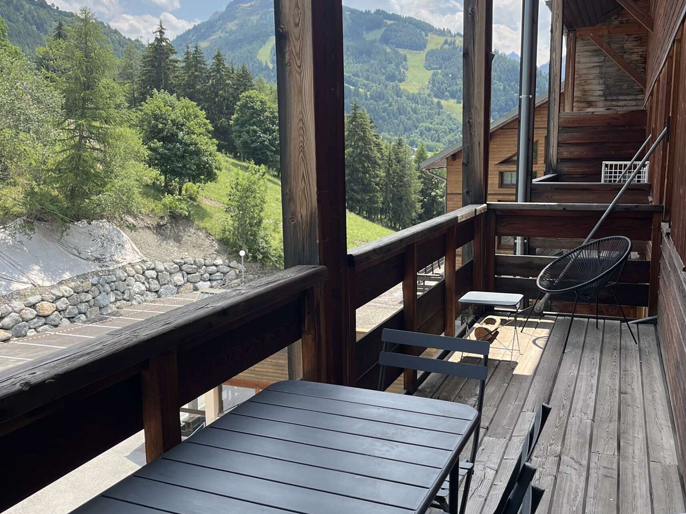 Eine Holzterrasse mit Tisch und Stühlen mit Blick auf eine gebirgige Landschaft.