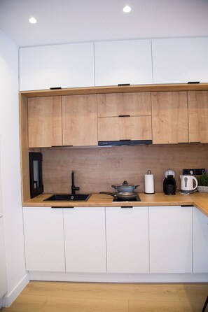 A modern kitchen with white cabinets, a wooden countertop, a sink, a stove, and a coffee maker. - Mocha Acropolis View Apartment (Athina)