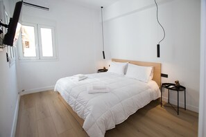 A neatly made bed with white bedding, a wooden headboard, and a bedside table with a small decorative item. - Mocha Acropolis View Apartment (Athina)
