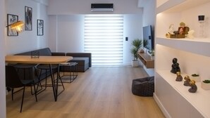 Un salon moderne comprenant un canapé, une table à manger avec des chaises, un téléviseur et une étagère ornée d’objets décoratifs.