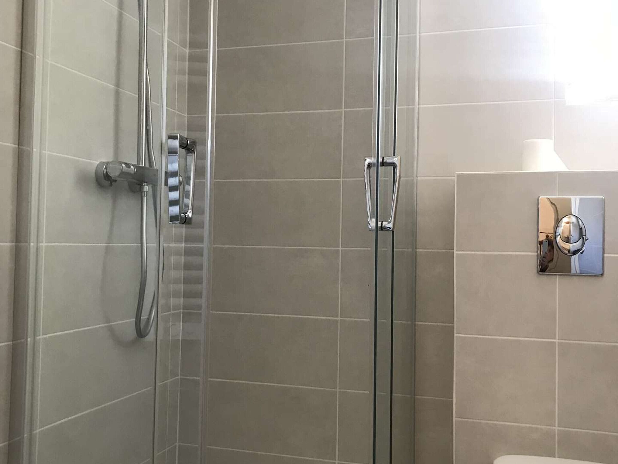 Un bagno moderno con doccia vetro, un water e un rubinetto a parete.
