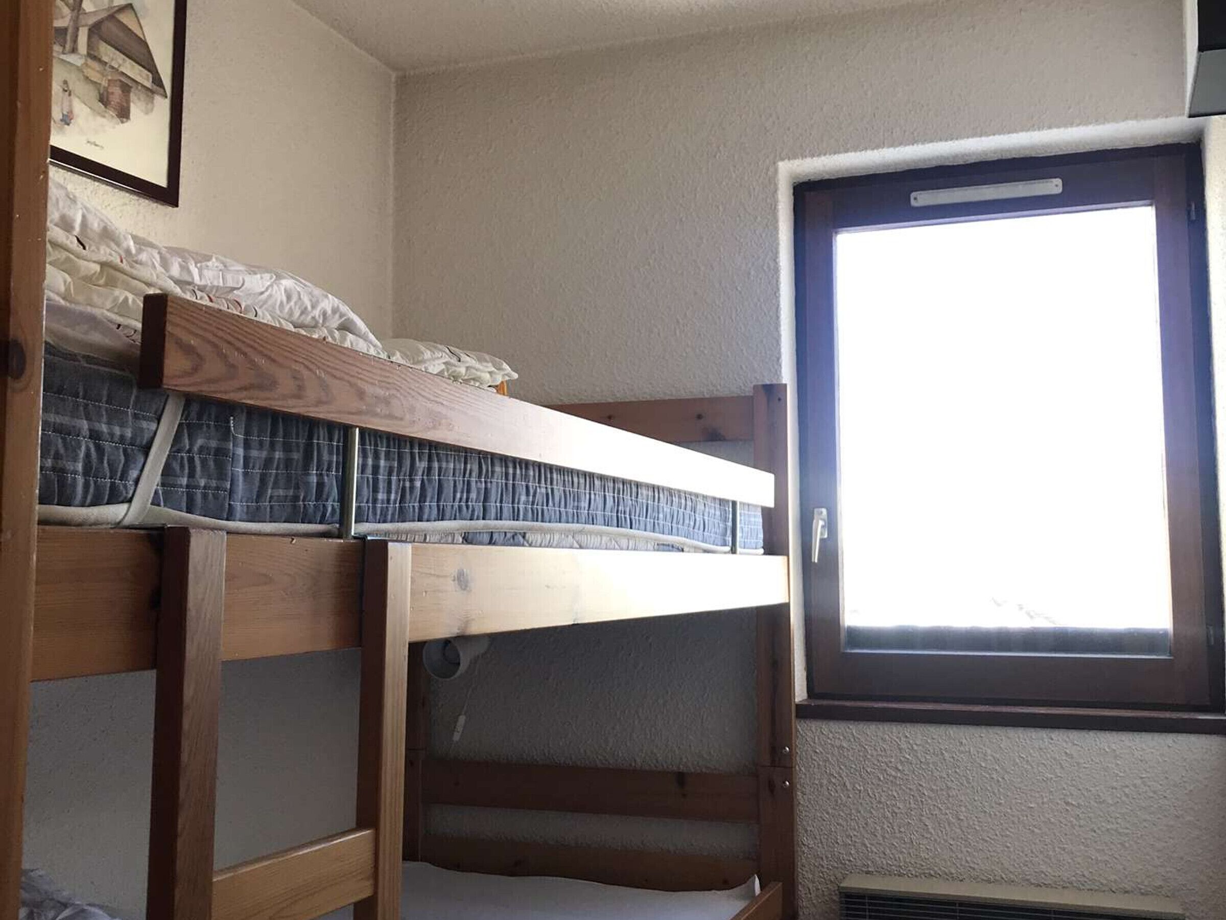A bunk bed with a window, a radiator, and a framed picture on the wall.