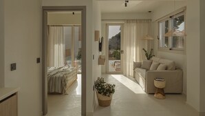 Un salon moderne avec un canapé, une petite table d’appoint, une plante en pot et une vue sur l’extérieur grâce à une porte vitrée.