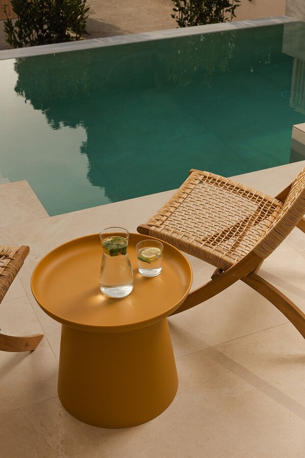 A poolside setting with a wicker chair, a small round table, and a bottle of water.