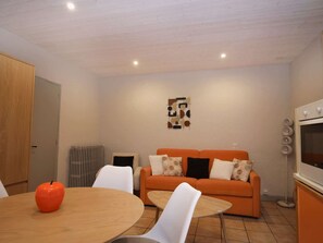 Ein modernes Wohnzimmer mit Holztisch, orangefarbenem Sofa und weißen Sesseln.