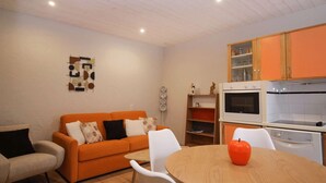 Ein kompakter Wohnbereich mit einer Couch, einem Esstisch und einer Küchenzeile inklusive Herd und Backofen.