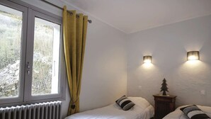 Ein Schlafzimmer mit zwei Einzelbetten, einem Heizkörper, einem Fenster mit gelben Vorhängen und zwei Wandleuchten.