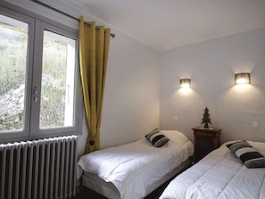 Ein Schlafzimmer mit zwei Einzelbetten, einem Heizkörper, einem Fenster mit gelben Vorhängen und zwei Wandleuchten.
