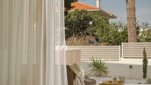 A room with a view of a swimming pool, a table with a book and a glass, and a chair with a cushion. - Luxury Suite with Private Pool by Kiva (Mitikas)