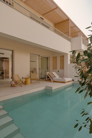 Un espace piscine extérieur moderne, doté de chaises longues, d’une petite table et d’un escalier menant à un balcon situé au deuxième étage.