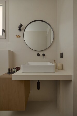 Ein modernes Badezimmer mit einem weißen Waschbecken, einem runden Spiegel und einem Holzkästen.