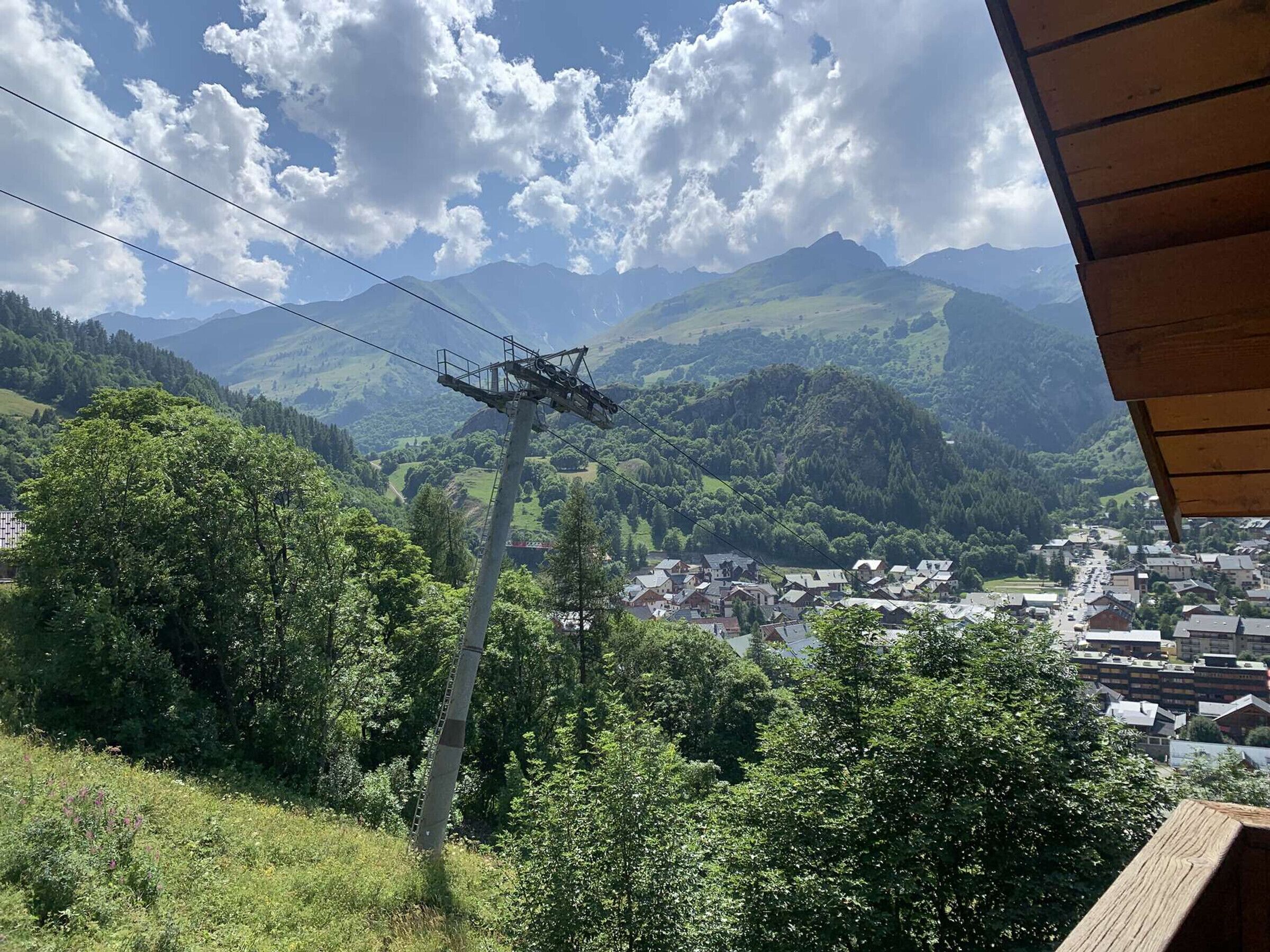 Un paysage montagneux avec un village en contrebas, une ligne électrique et une structure en bois au premier plan.