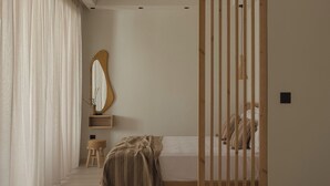 A minimalist bedroom with a bed, a bedside table, a mirror, and a window with curtains. - Luxury Suite with Balcony by Kiva (Mitikas)