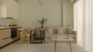 A modern kitchen with wooden cabinets, a dining table with chairs, a sofa, and a small table with a vase. - Luxury Suite with Balcony by Kiva (Mitikas)