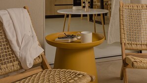 A cozy room with wicker furniture, a small round table, and a view into a kitchen area. - Luxury Suite with Balcony by Kiva (Mitikas)
