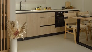 A modern kitchen with light wood cabinets, a black countertop, and a dining area with wooden chairs. - Luxury Suite with Balcony by Kiva (Mitikas)