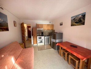 A compact kitchen with wooden cabinets, a refrigerator, and a microwave. There is a small dining area with a table and chairs. - Practical studio cabin - 4 guests (Valloire)
