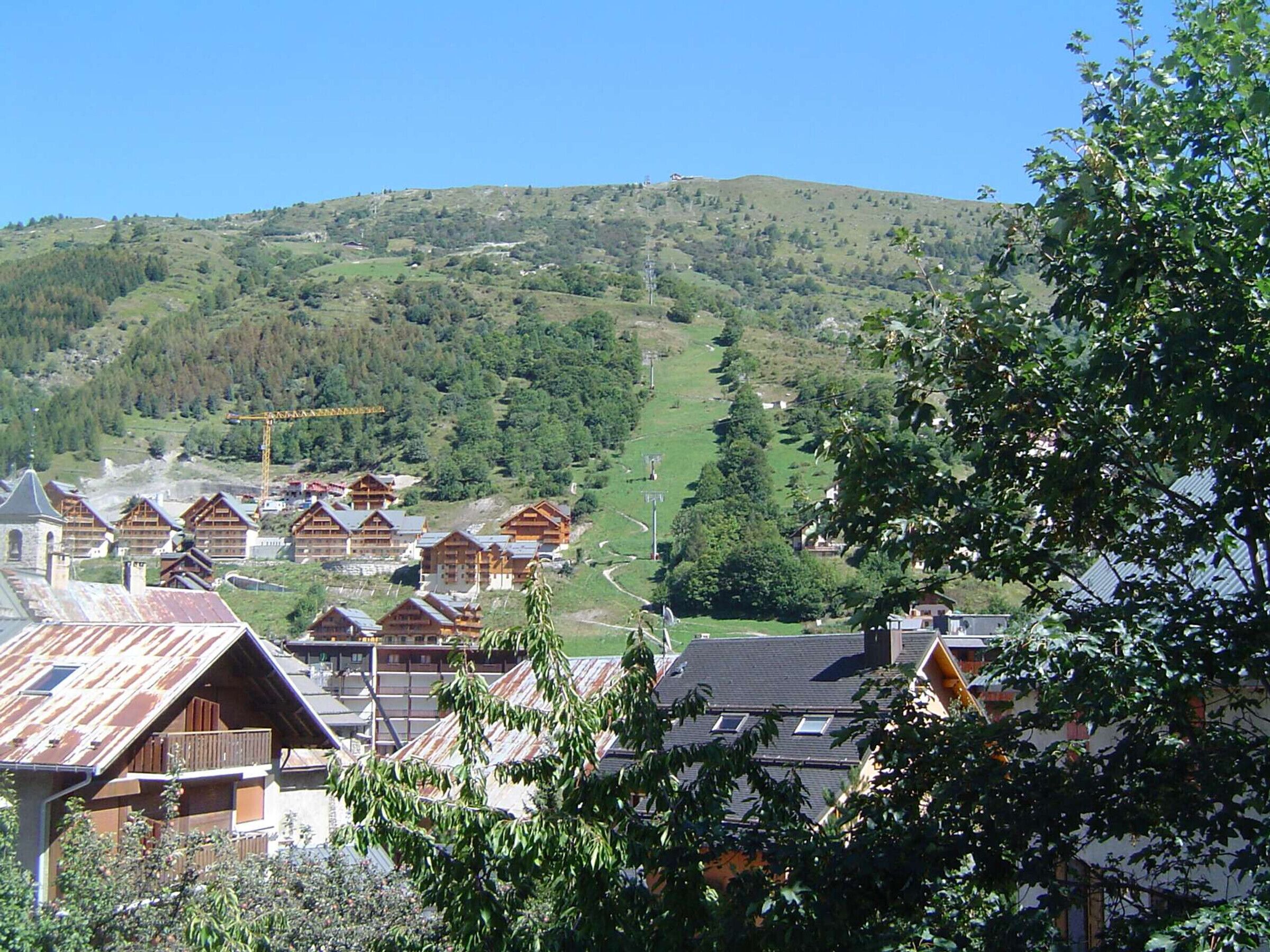 Un complejo turístico de montaña con edificios de estilo chalet, un telesilla y vistas de las colinas circundantes.