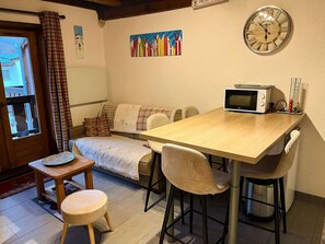 Ein gemütliches Zimmer mit einem Holztisch, einer Couch, einem kleinen Hocker, einer Mikrowelle und einer Wanduhr.