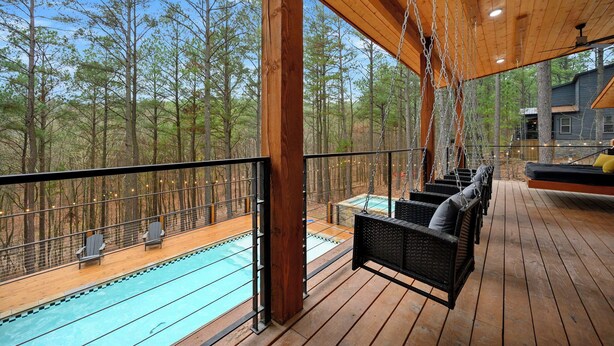 Una terraza de madera con piscina, sillas de mimbre y un columpio colgante.