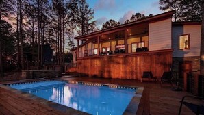 Una casa moderna con piscina, terraza de madera y amplios ventanales con vistas a un área boscosa.