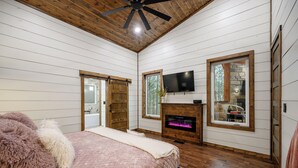 Un dormitorio con cama, chimenea, televisión y ventanas amplias.
