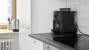 A modern kitchen with a Krups coffee machine on a countertop, a window with blinds, and a white radiator. - Grand Apartment close to the Isar and Citycenter (München)
