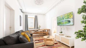 A modern living room with a sofa, a coffee table, a TV, and a dining area. - Grand Apartment close to the Isar and Citycenter (München)