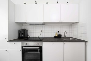A modern kitchen with white cabinets, a black countertop, a built-in oven, a coffee maker, and a sink.