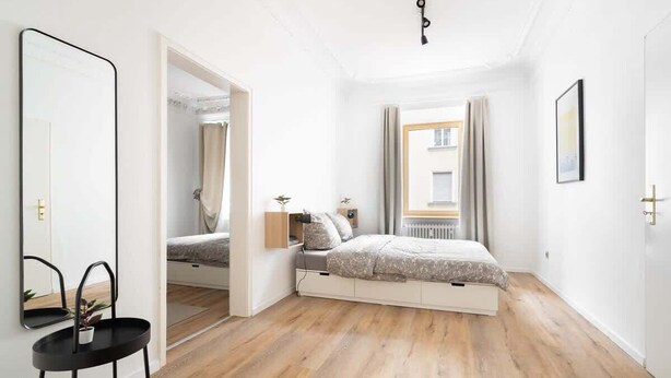 A bedroom with a bed, a bedside table, a mirror, and a window with curtains. - Grand Apartment close to the Isar and Citycenter (München)