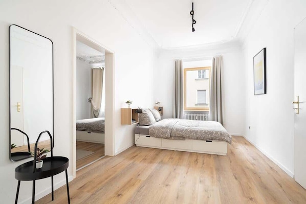 Ein Schlafzimmer mit Bett, Nachttisch, Spiegel und einem Fenster mit Vorhängen.