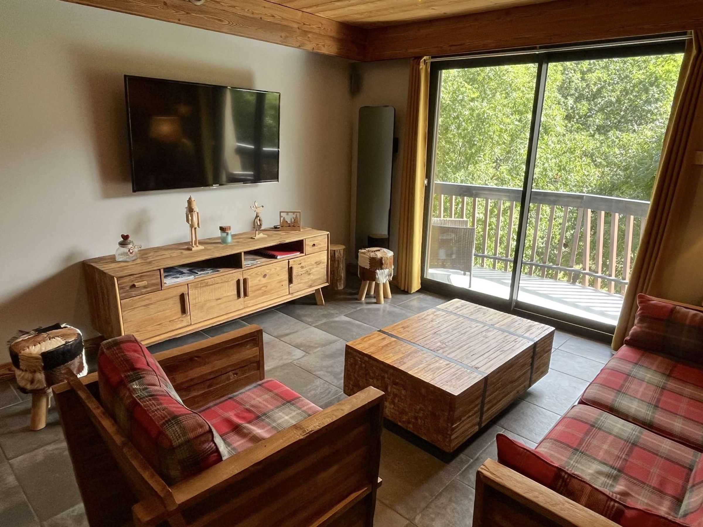 Un salon comprenant un meuble TV en bois, un canapé, une table basse et un balcon avec vue sur les arbres.