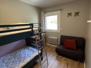 Ein kleines Zimmer mit Stockbetten, einer Schlafcouch, einem Fenster mit Vorhängen und einer Heizung.