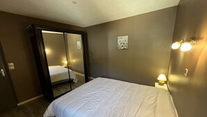 A bedroom with a bed, a mirror, a nightstand with a lamp, and a wall-mounted light fixture. - Spacious apartment with balcony - 7 guests (Valloire)