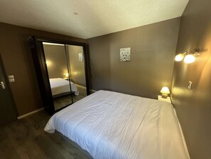 A bedroom with a bed, a mirror, a nightstand with a lamp, and a wall-mounted light fixture. - Spacious apartment with balcony - 7 guests (Valloire)