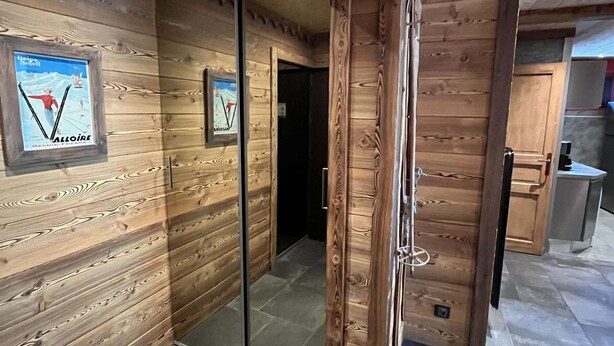 A wooden interior with a sliding glass door, framed posters on the wall, and a visible kitchen area. - Spacious apartment with balcony - 7 guests (Valloire)